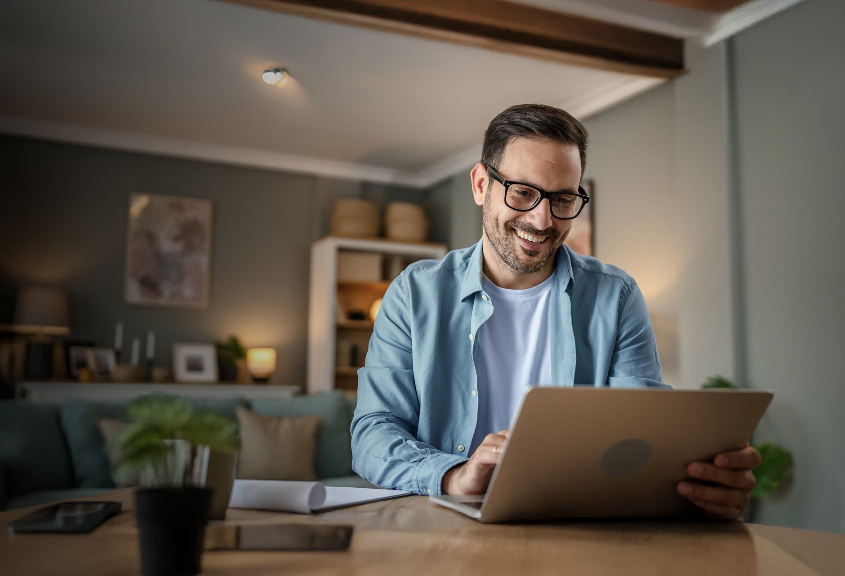 Mann sitzt am Tisch vor aufgeklapptem Laptop