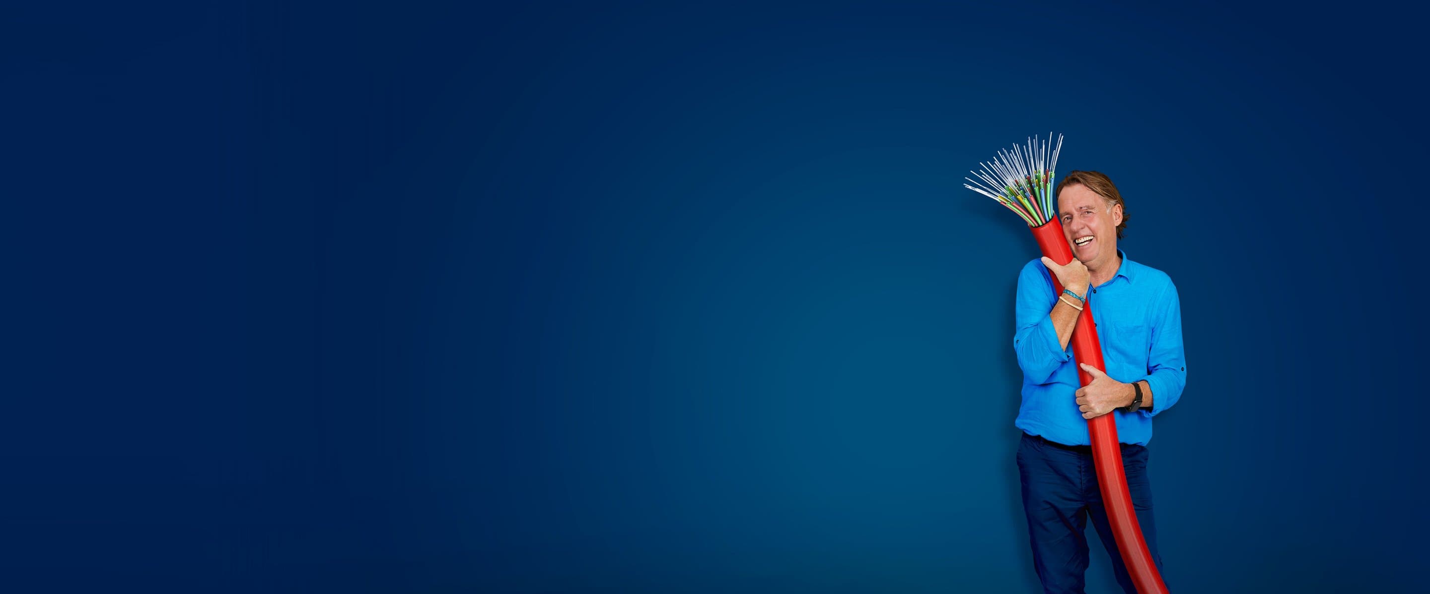 Eine Person in blauem Hemd hält ein großes rotes Kabel mit freiliegenden Glasfasern vor einem einfarbig blauen Hintergrund.